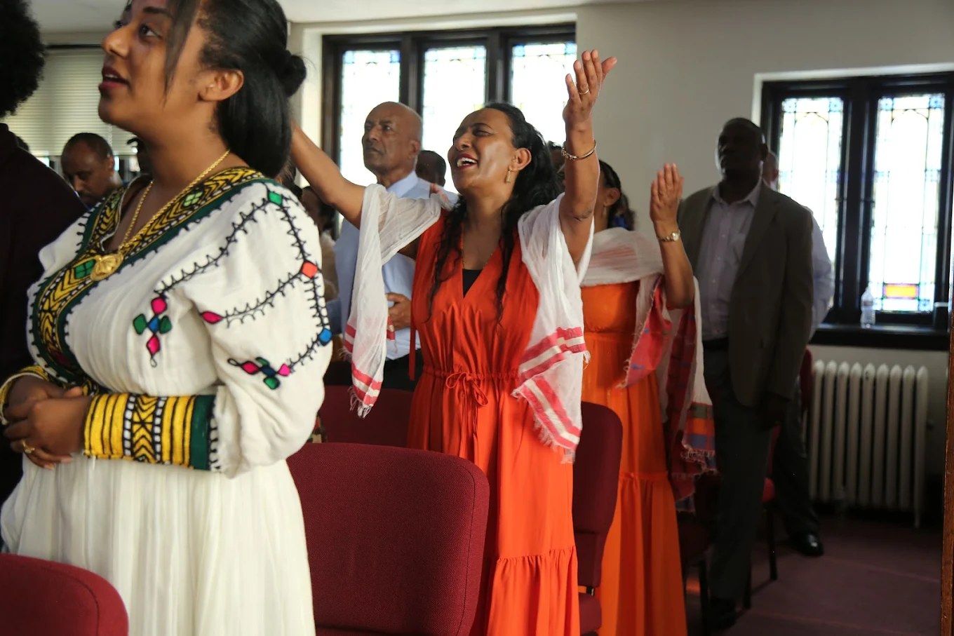People worshiping with hands raised during the Amharic service